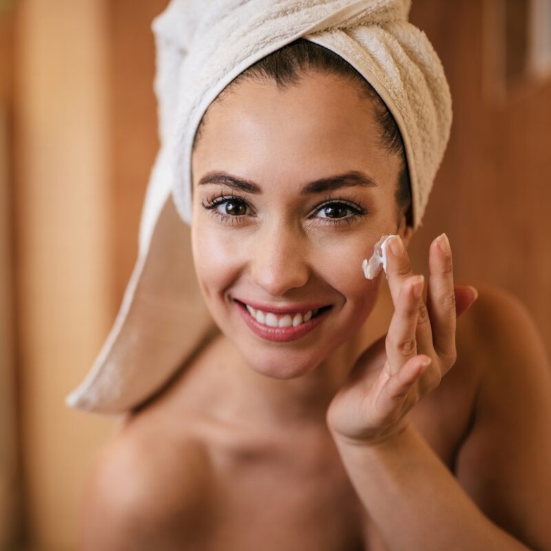 Beautiful woman applying moisturizer on her face in the bathroom.